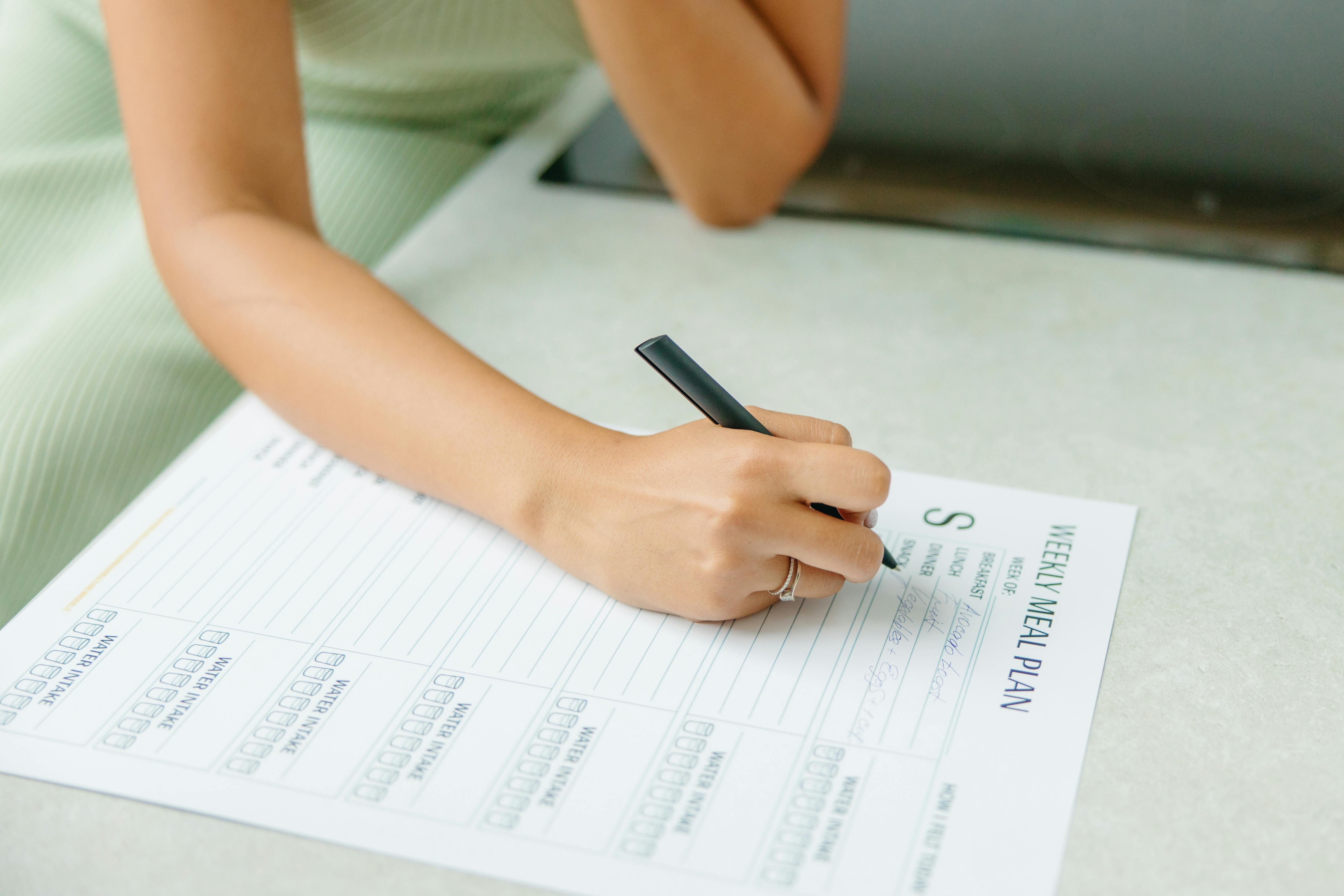 Woman Planning Weekly Meals: Organized and Nutritious Meal Preparation A woman planning her weekly meals at a kitchen table with a notebook and fresh ingredients.