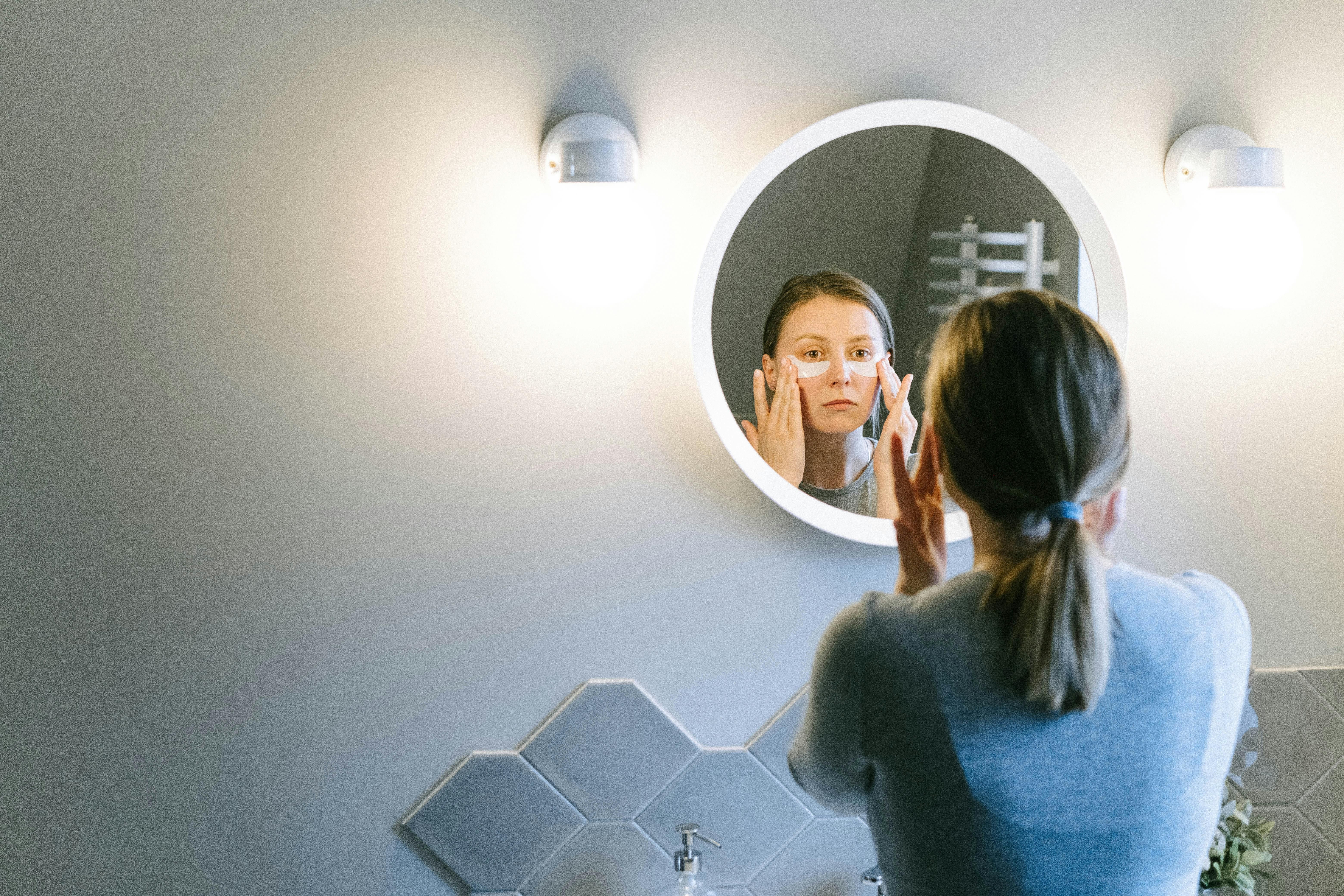 Woman Using Night Cream and Eye Patches in Skincare Routine for Radiant Beauty Sleep A woman applying night cream and under-eye patches as part of her nighttime skincare routine to rejuvenate and hydrate her skin before sleep.