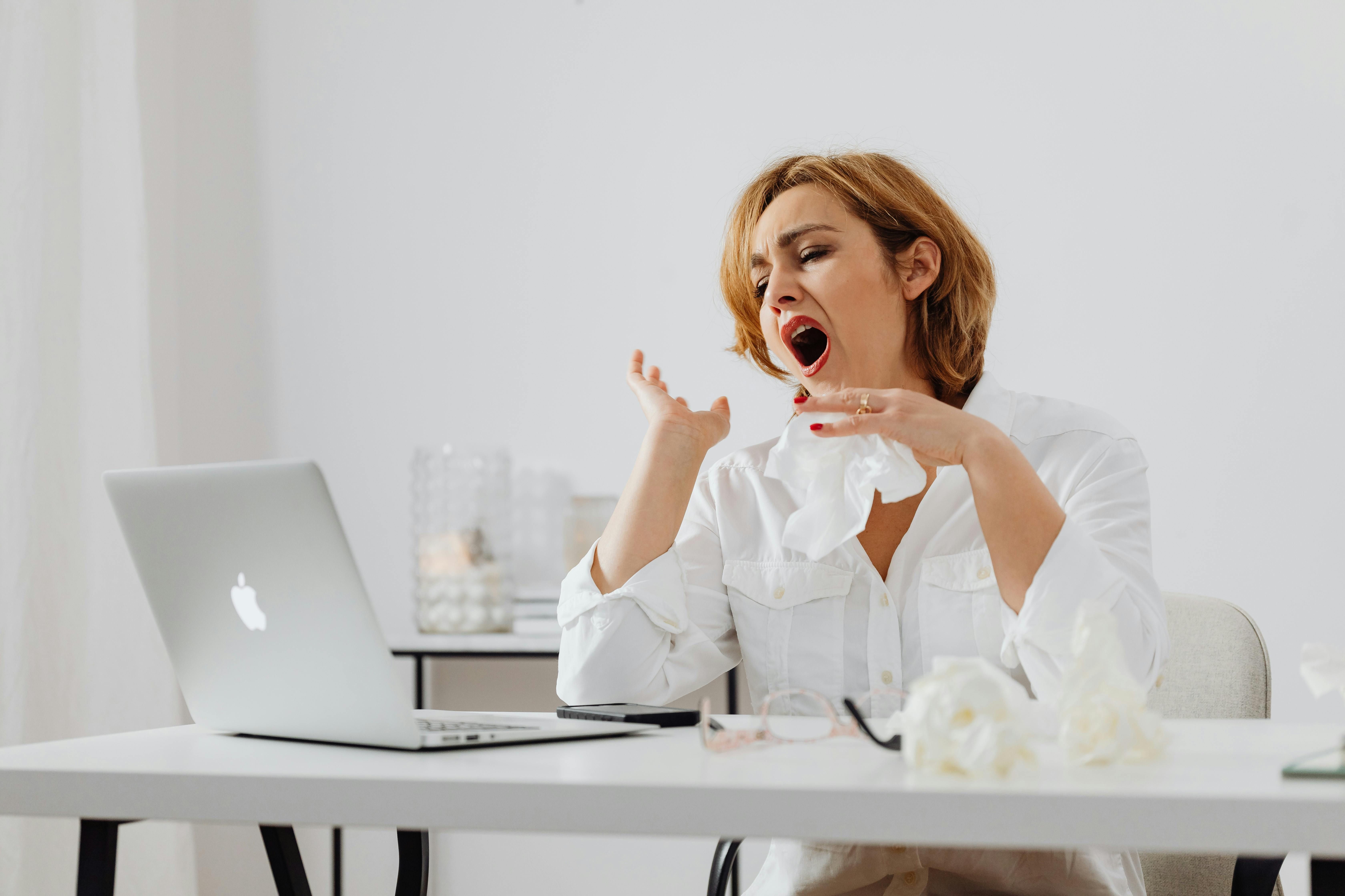 Fighting Afternoon Fatigue: Woman Yawning at Work Due to the Afternoon Crash A woman yawning at her desk while working on her computer, experiencing an afternoon energy slump.